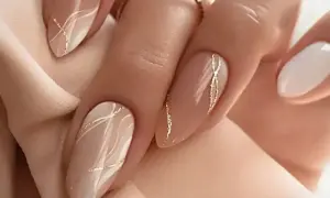 Elegancki, modny manicure w odcieniach beżu i bieli, ozdobiony złotymi, falistymi liniami.