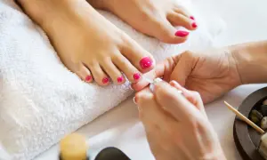 Pedicure paznokcie u nóg w intensywnym różu. Dłonie kosmetyczki precyzyjnie malują paznokcie, tworząc letni look.
