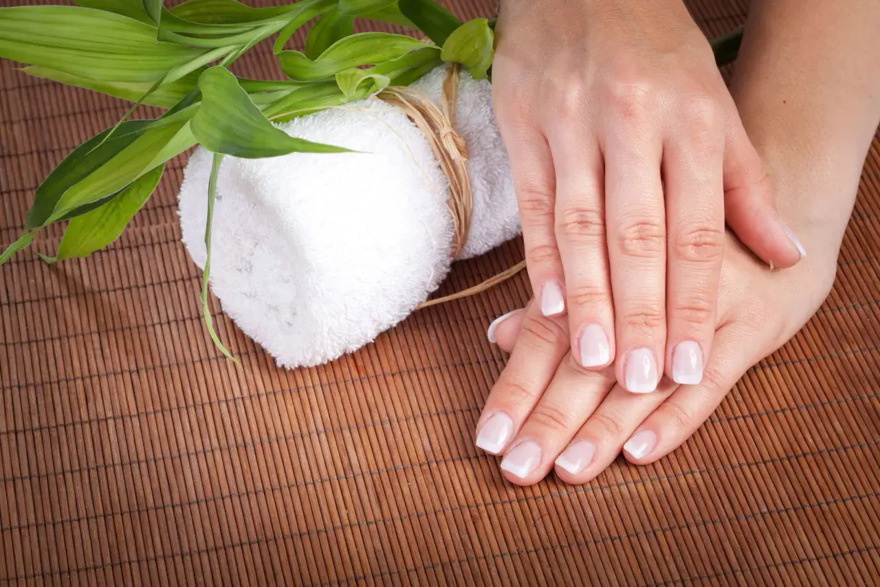 Delikatne dłonie z francuskim manicure, biały ręcznik i zielone liście bambusa. Czy to jest manicure japoński?
