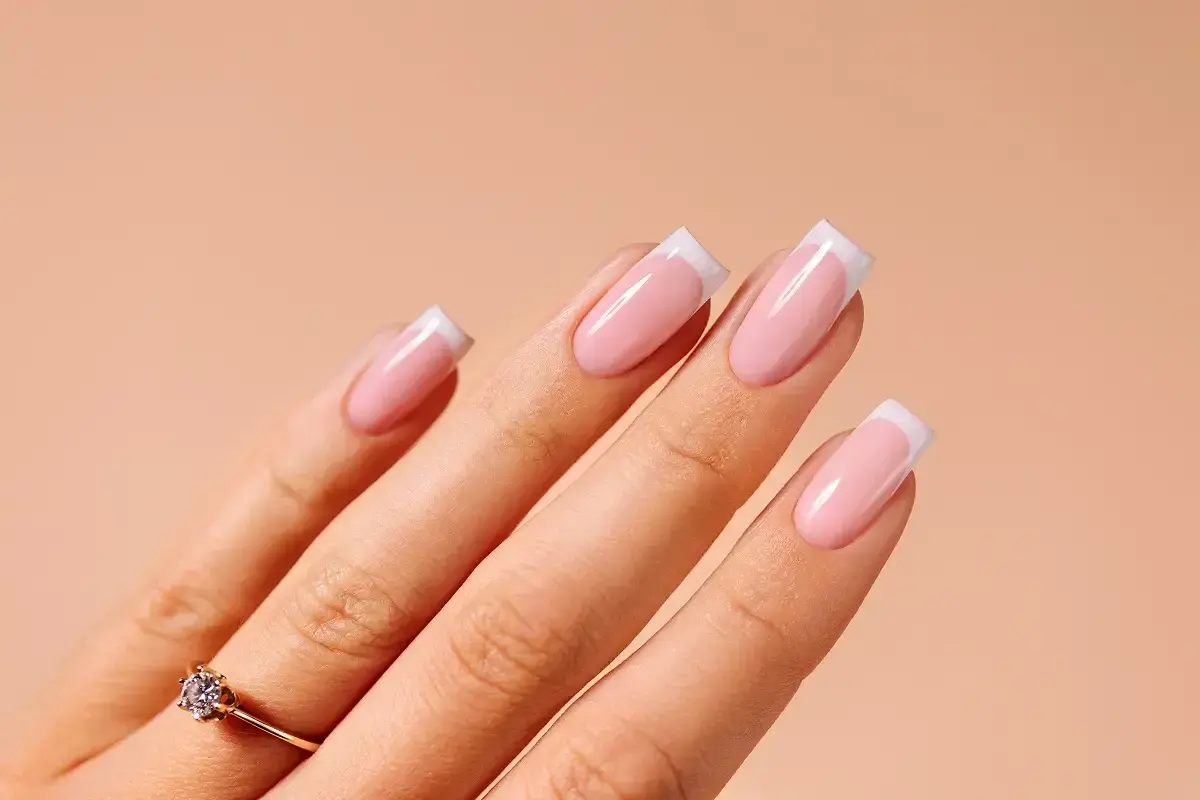 Dłoń z paznokciami w stylu french ze wzorkiem. Delikatny róż i biel tworzą klasyczny, elegancki manicure.