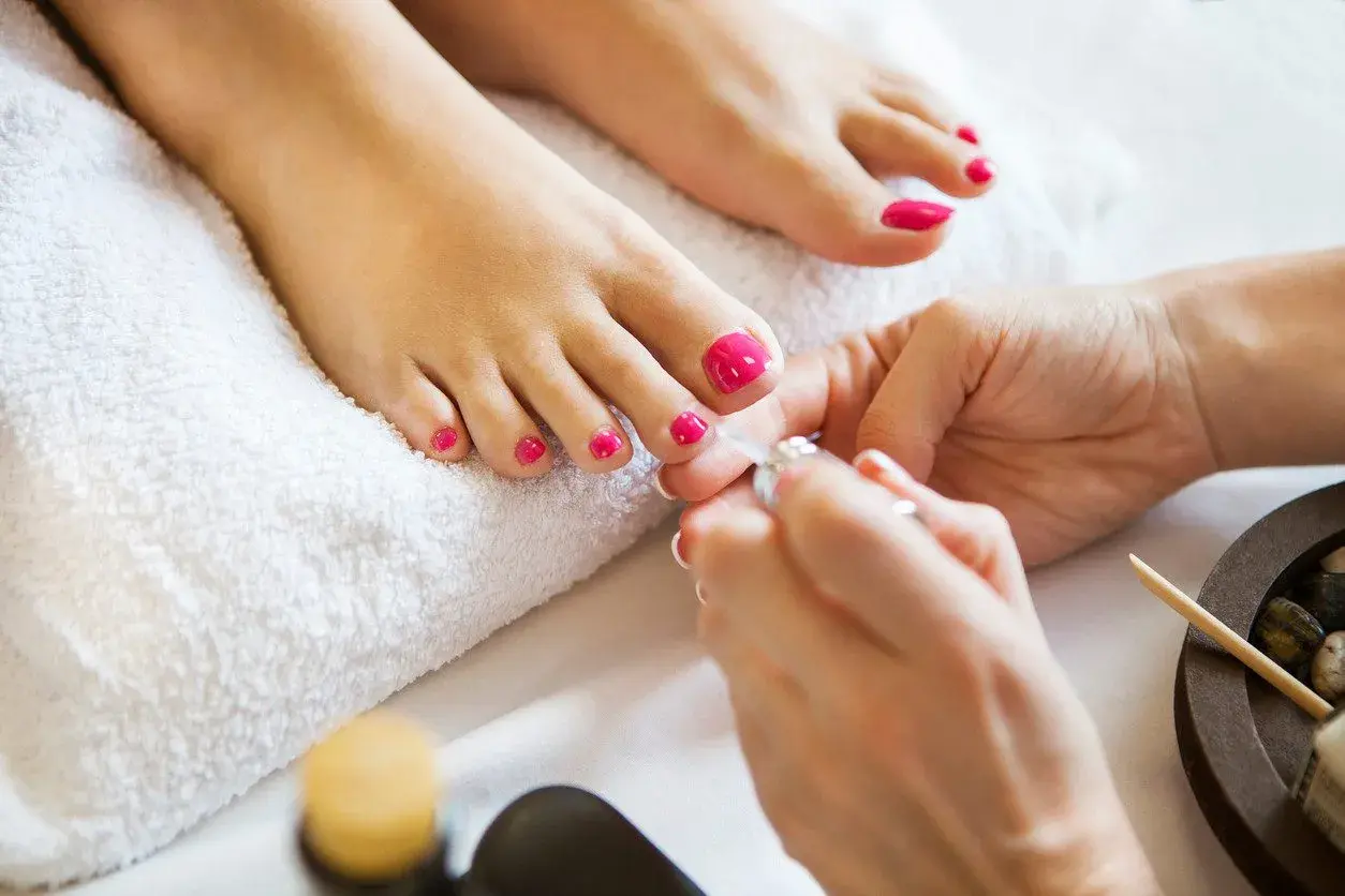 Pedicure paznokcie u nóg w intensywnym różu. Dłonie kosmetyczki precyzyjnie malują paznokcie, tworząc letni look.